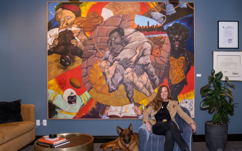 Katy Durant and dog in front of a Robert Colescott painting. 