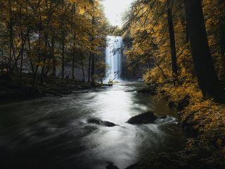 A Waterfall With Trees On The Side Of A River